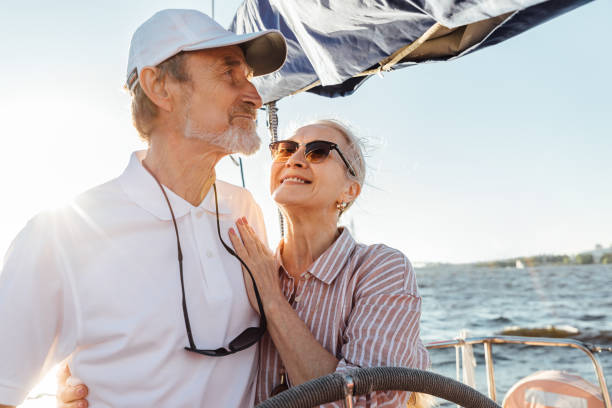 istock Happy mature woman looking on her husband while he steering a yacht. Affectionate couple enjoying a vacation on private sailboat at sunny day. 1271336729