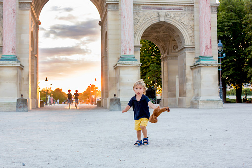 Cute toddler boy, playing with teddy bear, visiting Paris during the summer on sunset