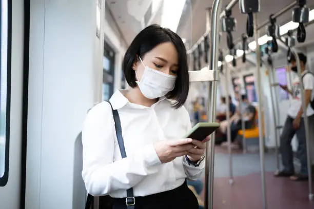 Asian woman wearing an anti-virus mask uses a smartphone to travel on a subway train as a COVID-19 outbreak occurs in the country.
