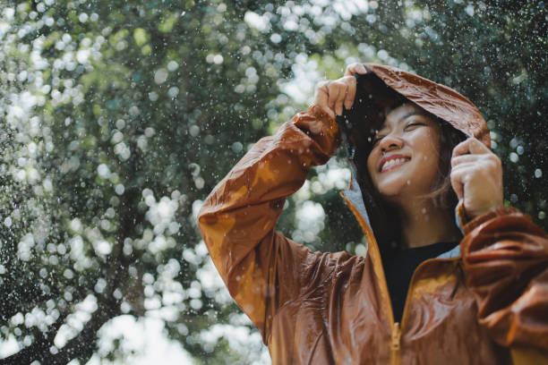 屋外でレインコートを着たアジア人女性。彼女は幸せです。 - umbrella women storm yellow ストックフォトと画像