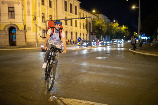 Delivery person cycling through city streets on his way to customer at night