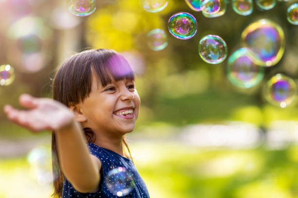 girl playing with soap bubbles outdoors - bubble child bubble wand blowing imagens e fotografias de stock