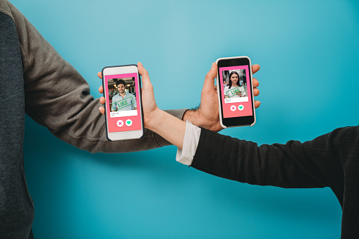 Conceptual image of two hands holding smart phones with an online dating app on the screen. Online dating app concept. Blue background.