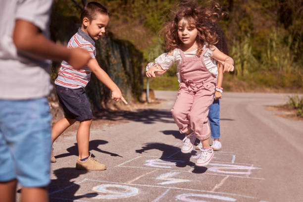 группа детей, весело играющих hopscotch на улице - hopscotch стоковые фото и изображения