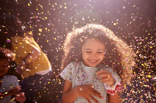 Portrait of confetti falling on little african-american girl with curly hair smiling looking down outdoors