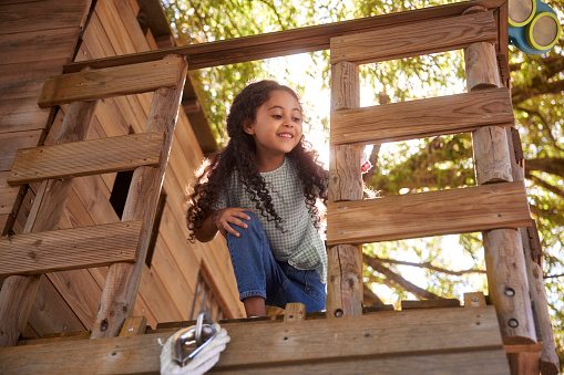 Young little african-american girl with curly hair smiling playing in tree house on summer day