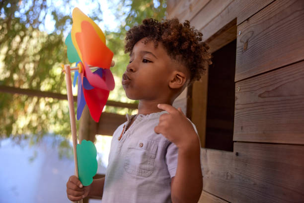 Little boy blowing colorful pinwheel on top of tree house