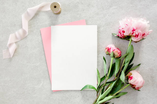 istock Mockup invitation, blank paper greeting card, pink envelope and peonies on gray stone table. Flower background. Flat lay, top view 1271345429