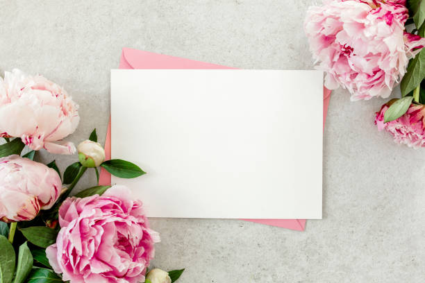 istock Mockup invitation, blank paper greeting card, pink envelope and peonies on gray stone table. Flower background. Flat lay, top view 1271345499