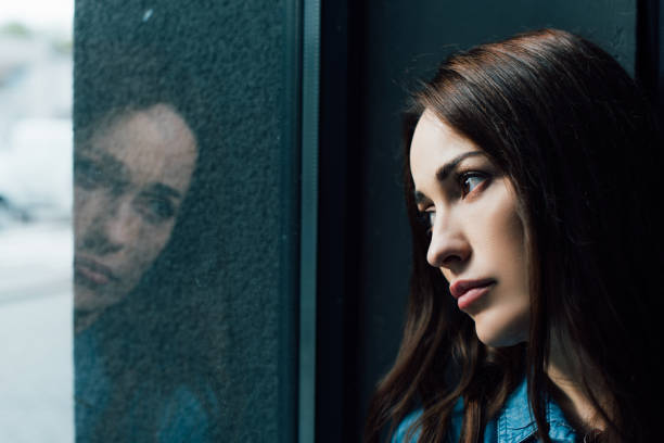 istock depressed and brunette woman looking at window 1271348148