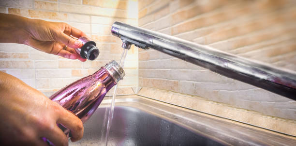 hand mit aluminium eco freundliche flasche gießen leitungswasser aus dem waschbecken, um kunststoffverbrauch zu reduzieren - sustainable resources water conservation water faucet stock-fotos und bilder