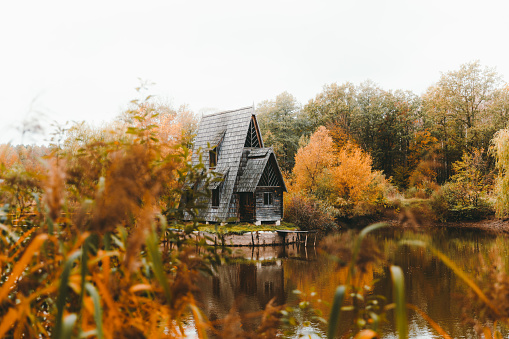 Dramatic view of the beautiful abandoned fishing cabin above the lake in the forest covered by the colorful autumn tones