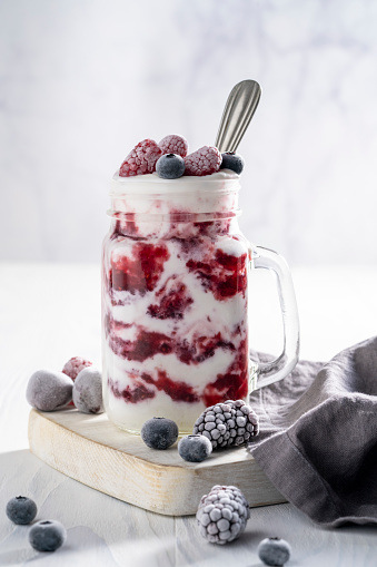Raspberries yogurt smoothie with frozen blueberries, blackberries and raspberries on a white table