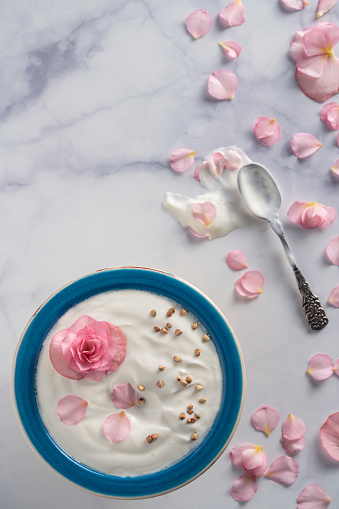 White yogurt blue bowl breakfast with edible pink begonia flowers on white marble table