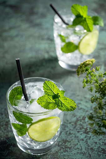 Mojito cocktail beverage with mint and lime slices on green background