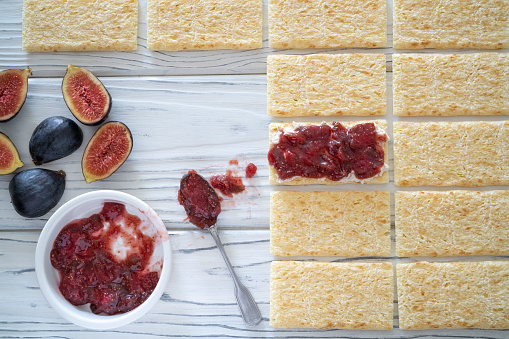 Figs jam homemade with fig fruits, cheese, nuts and bread toast slice on white rustic wooden background