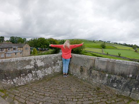 Rear view of a mid-adult woman standing with her arms outstretched looking at the view of the countryside in North Yorkshire.
