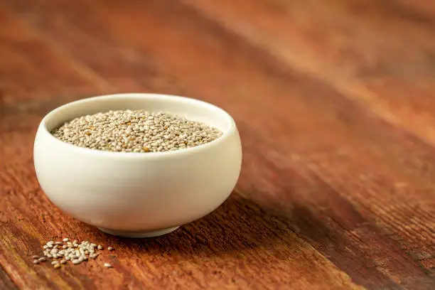 organic white chia seeds rich in omega-3 fatty acids,  a small ceramic bowl on weathered wood with a selective focus and copy space