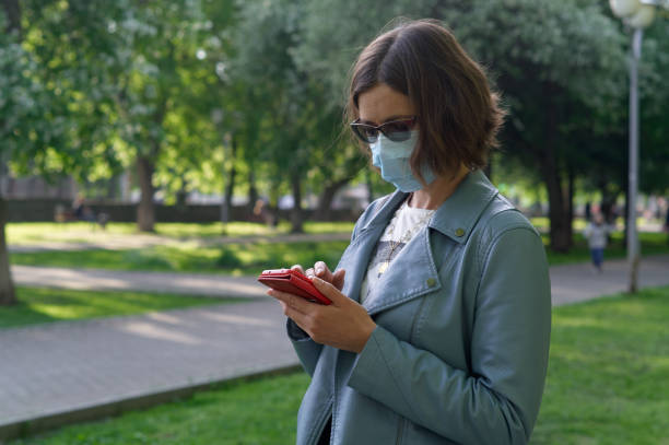 istock Young woman in protective mask using a smartphone in the park 1271353830