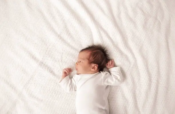 Cute newborn baby girl lying in the bed. Two weeks old infant child on white soft blanket.