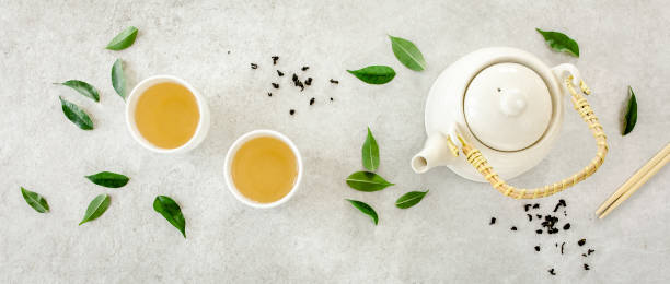 istock Herbal tea with two white tea cups and teapot, with green tea leaves. Flat lay, top view. Tea concept 1271359517
