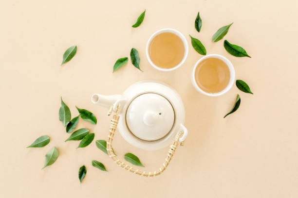 istock Herbal tea with two white tea cups and teapot, with green tea leaves. Flat lay, top view. Tea concept 1271360102