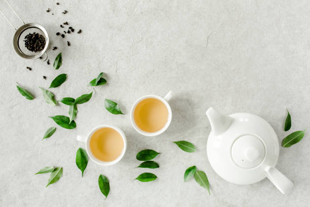 istock Herbal tea with two white tea cups and teapot, with green tea leaves. Flat lay, top view. Tea concept 1271367596