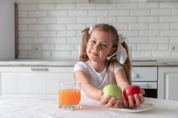 маленькая девочка с соком и фруктовыми яблоками на кухне. здоровой пищи. вегетарианство. ребенок ест растительную пищу. - apple eating little girls green стоковые фото и изображения