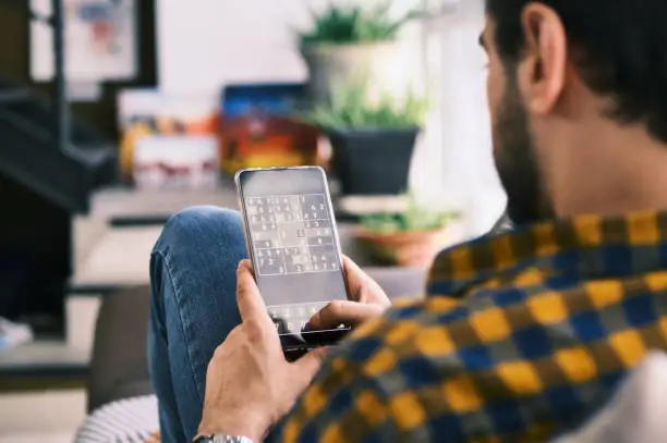Photo of Young Man Playing Sudoku Game With App On Smartphone