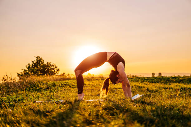 Young active woman making bridge yoga pose on meadow. Drone view.