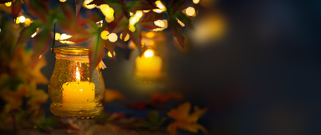 Festive autumn lighting decor. Candle in a jar with rain drop, hanging on tree branches for night decoration.