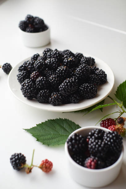 istock Composition from a white plate with fresh blackberries, scattered blackberries and green leaves on a light background 1271374582