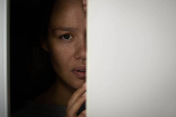Woman hiding in the closet afraid with worry in her eyes. Frightened woman hiding behind a closet door filipino ethnicity photos stock pictures, royalty-free photos & images