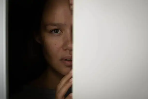 Frightened woman hiding behind a closet door