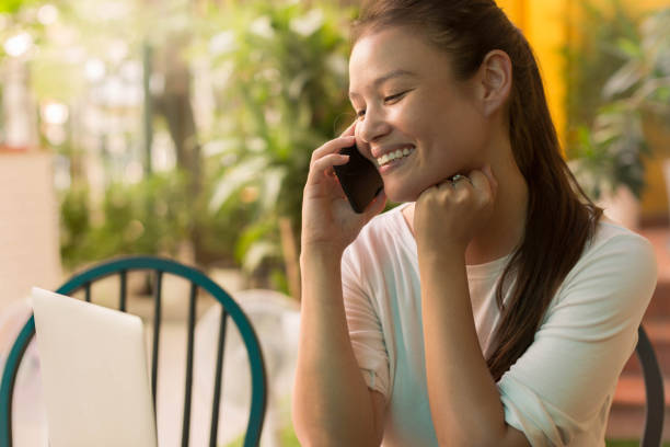 Business woman making a phone call for work at home, sitting at her computer. Pretty woman making a business call on her phone at home duirng the day, smiling and happy. hot filipina women stock pictures, royalty-free photos & images