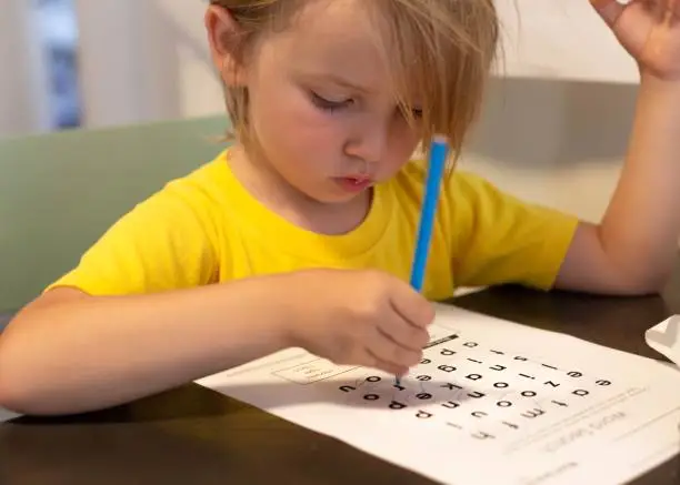 Photo of A young kid doing school work at home. Learning words.