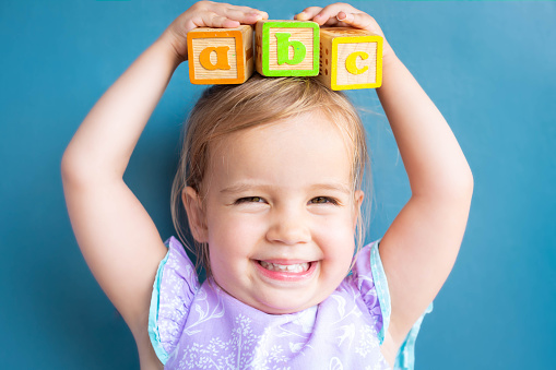 A cute little girl balancing abc alphabet blocks on her head playing in the classroom.