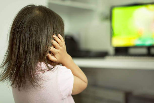 Little kid covering her ears, frightened from loud noise from TV. Autism. Sensitive kids afraid of loud sounds noise, in front of the tv covering ears in fear. sense of science and technology stock pictures, royalty-free photos & images