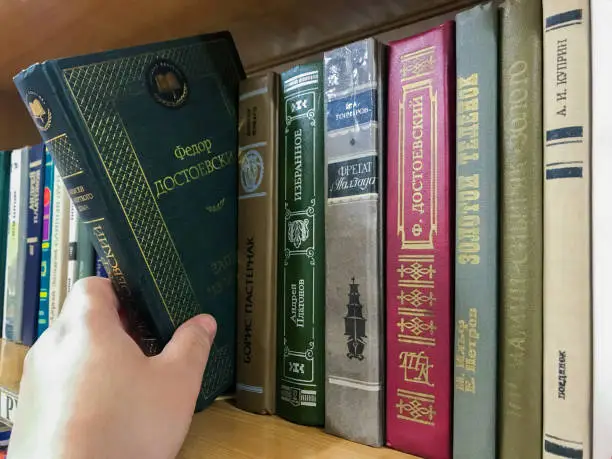 Moscow, Russia, August 2020: Close-up of a bookshelf with books by Russian writers. Hand pulls out Dostoevsky's book.