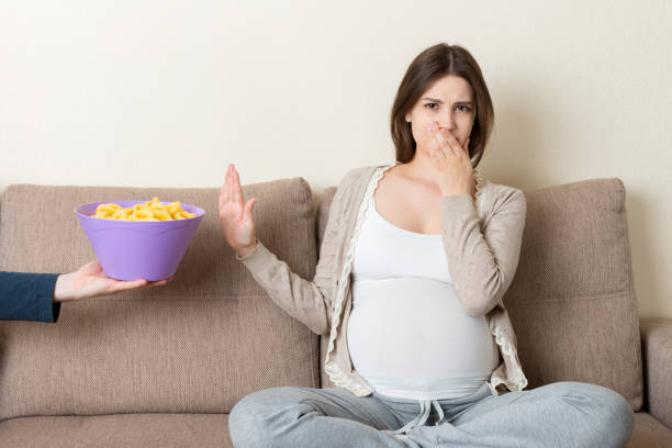 Pregnant woman sitting on the sofa refuses to eat unhealthy snacks. Stop to the junk food during pregnancy concept Pregnant woman sitting on the sofa refuses to eat unhealthy snacks. Stop to the junk food during pregnancy concept. family eating potato chips stock pictures, royalty-free photos & images