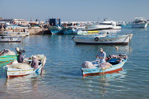 Alexandria, Egypt - December 14, 2018: Fishermen repair nets in boats at old fishing harbor of Alexandria