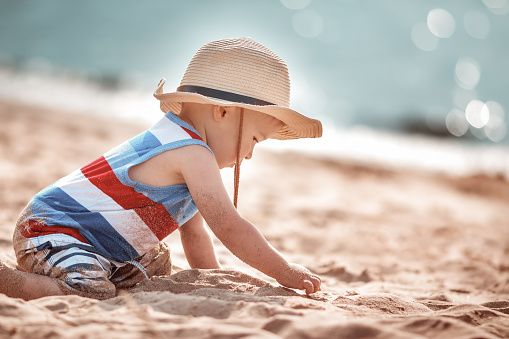one year old boy playing at the beach in straw hat. Child on family vacations at sea.