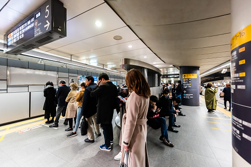 Shibuya, Japan - April 1, 2019: People standing waiting in line for metro railway car on platform during rush hour in underground indoors inside station in Tokyo