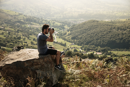 Young man taking a picture with a DSLR camera on the top of a mountain