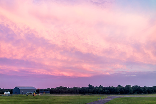 Dulles, USA - June 13, 2018: Dulles International Airport, IAD, runway view with colorful dramatic pink red sunset in Virginia field and building by military plane