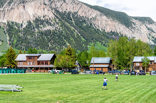Mount Crested Butte, USA - June 20, 2019: Colorado village in summer with town park and people playing soccer football sports on grass field in downtown by houses buildings