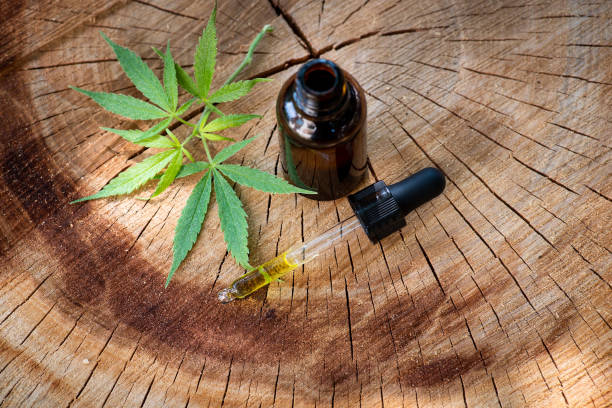 Cannabis medical oil in a small bottle on a natural wooden log Cannabis medical oil in a small bottle and marijuana leaves on a natural wooden log, alternative herbal medicine thc photos stock pictures, royalty-free photos & images