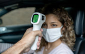 Woman in her car getting her temperature checked with an infrared thermometer