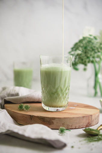 Iced Green matcha tea and pouring milk in crystal glass on wood plank. Part of a series