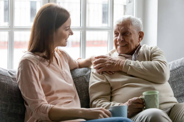 Smiling young woman enjoying talking to happy old father. Smiling young woman sitting on sofa with happy older retired 70s father, enjoying pleasant conversation with cup of coffee tea together in living room, mature parents and grown children communication. seniors talking stock pictures, royalty-free photos & images